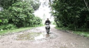 Seorang pengendara sepeda motor melintasi jalan yang rusak di Kecamatan Panyabungan Barat